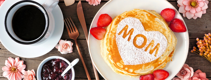 Mothers Day breakfast pancakes with heart shape and MOM letters, overhead view table scene on rustic wood stock photo