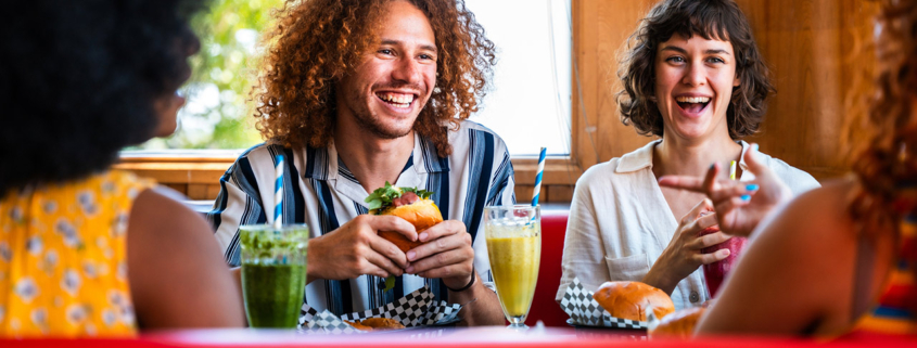Multiethnic friends bonding, eating burgers and laughing in a diner stock photo