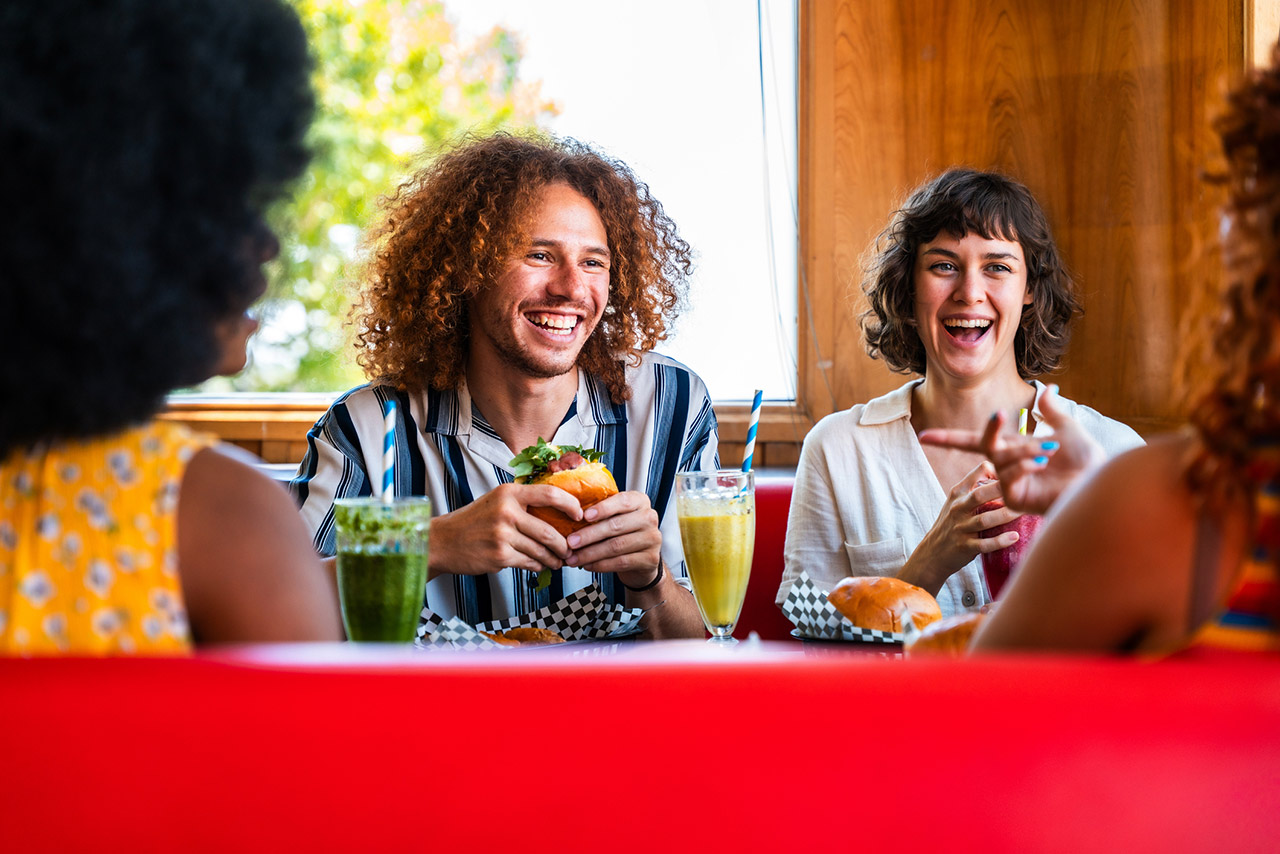 Multiethnic friends bonding, eating burgers and laughing in a diner stock photo