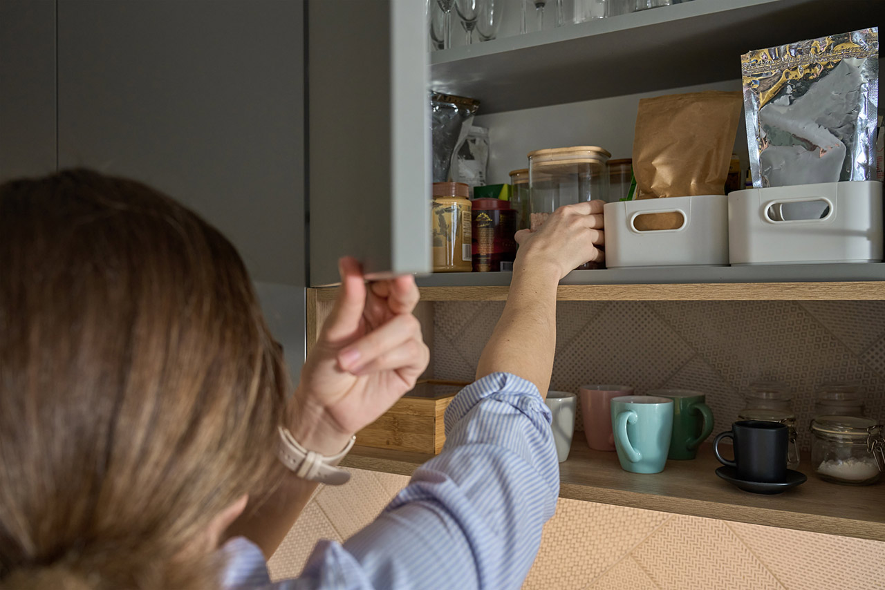 Woman reaching for jar in kitchen cabinet with stored cooking ingredients stock photo