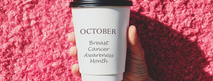 Hand holding white paper cup with October Breast Cancer Awareness Month lettering