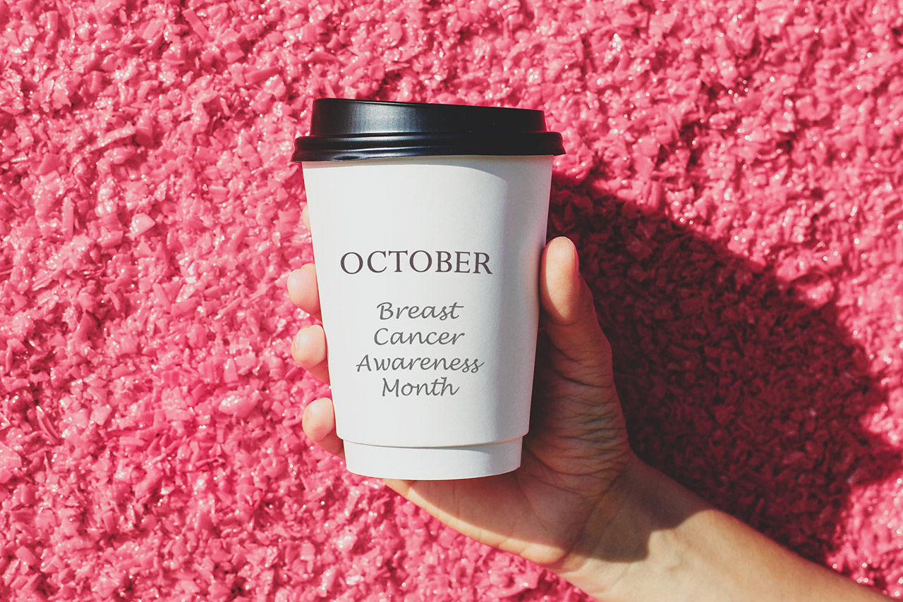 Hand holding white paper cup with October Breast Cancer Awareness Month lettering